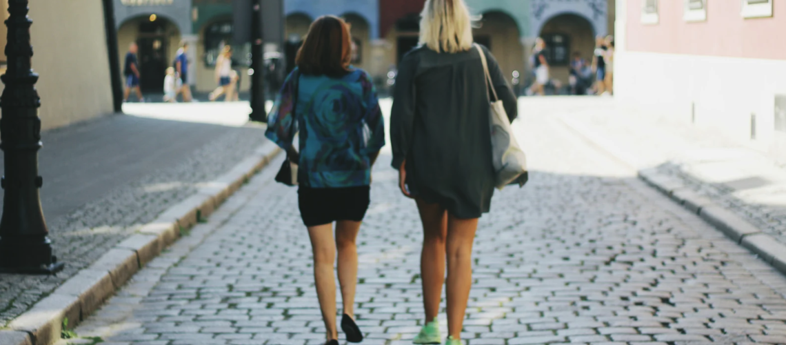 Two women walking side by side down a cobblestone street, representing relational healing, community, and the hidden realities of sex trafficking demand.